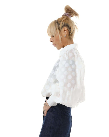 Model wearing a white sheer polka dot shirt with puff sleeves, showcasing a stylish side profile.