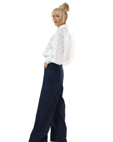 Model wearing a white sheer polka dot puff sleeve shirt with denim wide-leg pants, showcasing a stylish outfit.