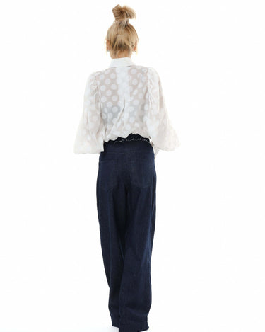Back view of a white sheer polka dot puff sleeve shirt paired with high-waisted denim trousers.