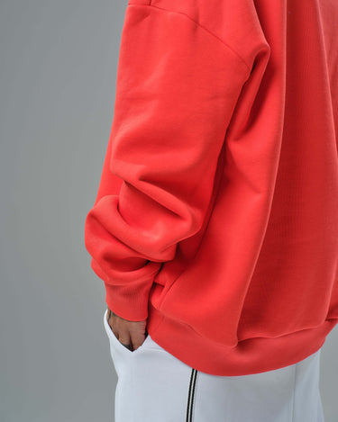 Detail of a red oversized sweatshirt sleeve paired with white joggers, showcasing stylish urban fashion.