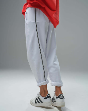 Close-up of white joggers with black stripes, featuring rolled cuffs, paired with a bold red oversized sweatshirt.