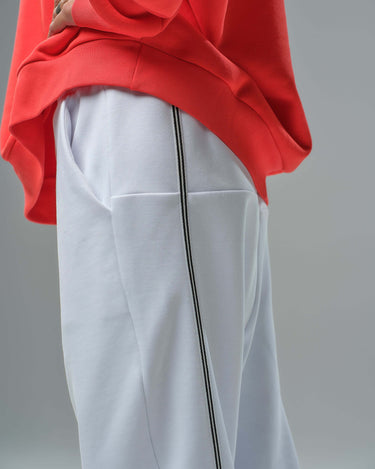 Person wearing a bold red oversized sweatshirt and white joggers with side stripes, showcasing urban streetwear style.