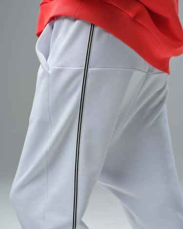 Close-up of white joggers with black stripes, paired with a red oversized sweatshirt, stylish urban streetwear.