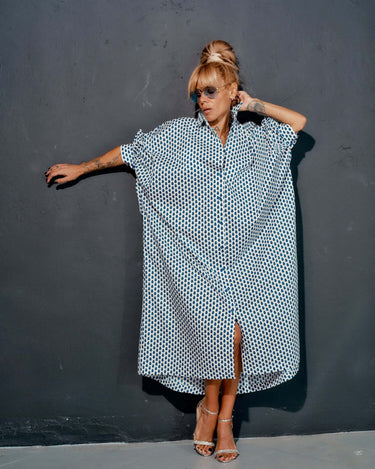 Woman wearing an oversized shirt dress with a blue micro floral print, styled with sunglasses against a dark wall.