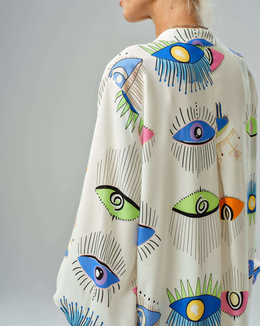 Side view of a model wearing a vibrant eye print shirt dress with a loose fit and ¾ sleeves.