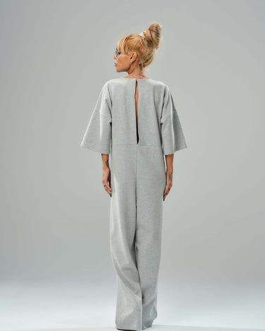 Grey wide-leg jumpsuit with open back, featuring cropped sleeves and a bold slit, showcasing modern style.