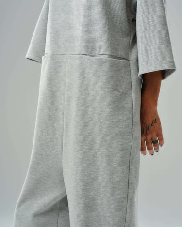 Side view of a grey wide-leg jumpsuit with open back and cropped sleeves, highlighting side pockets and relaxed fit.