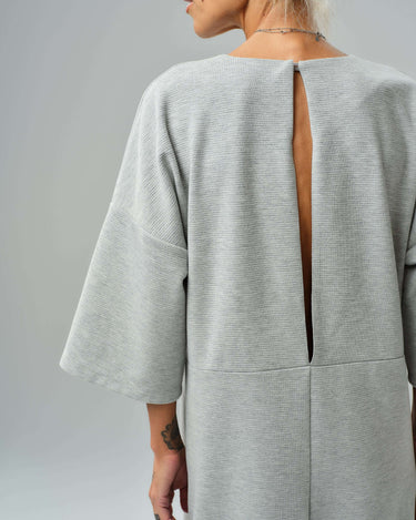 Back view of a grey wide-leg jumpsuit featuring an open slit back and cropped sleeves, showcasing its modern design.