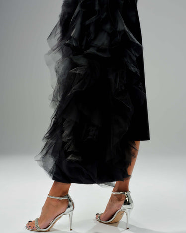 Side view of a model wearing a black tulle detail blazer with dramatic tulle accents and silver high-heeled sandals.