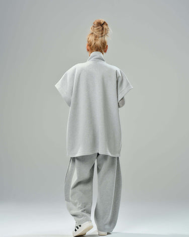 Back view of a woman in an oversized grey three-piece set with wide-leg trousers and a sleeveless vest.