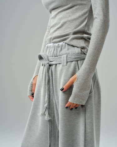 Model wearing oversized grey three-piece set featuring drawstring trousers and fitted long-sleeve top.
