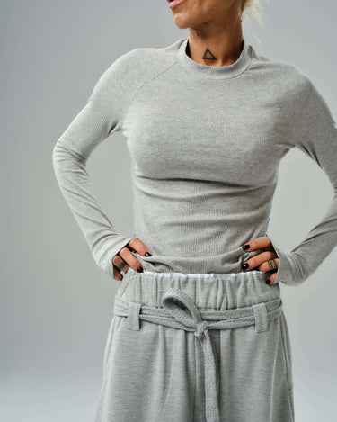Woman wearing a fitted long-sleeve ribbed top with wide-leg drawstring trousers in a classic gray three-piece set.
