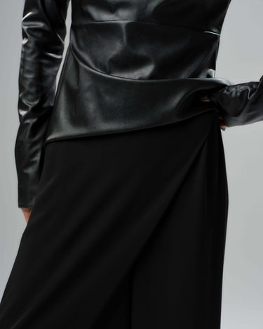 Close-up of a black faux leather top with structured silhouette and cut-out shoulder details, styled with a sleek black skirt.