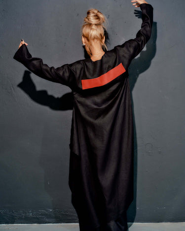 Back view of a woman wearing a black tunic with a red leather stripe, showcasing modern minimalist fashion.