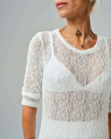 Close-up of a woman wearing a sheer white tunic with textured fabric and a stylish neckline.