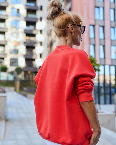 Woman in a red oversized sweatshirt showcasing urban style against a modern city backdrop.