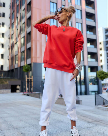 Model wearing a bold red oversized sweatshirt and white jogger set in an urban setting.