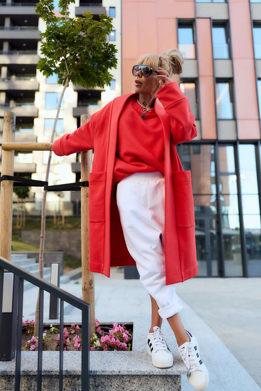 Model wearing a red oversized coat with side pockets, styled casually with white pants and sneakers.