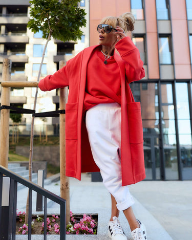 Model wearing a red oversized coat with side pockets, styled casually with white pants and sneakers.