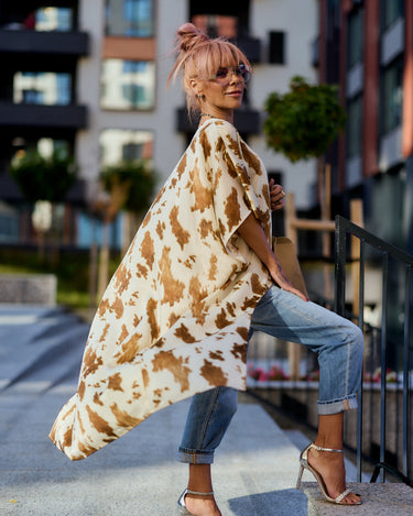 Woman wearing a Beige Printed Asymmetric Tunic with camel-toned abstract print, styled over jeans.