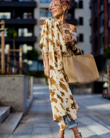 Woman wearing a Beige Printed Asymmetric Tunic with a camel-toned abstract print, styled with jeans and a tote bag.
