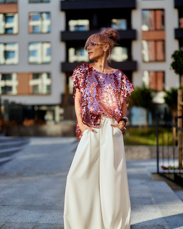 Model wearing Pink Sequin Oversized Top with wide pants in urban setting, showcasing modern eveningwear style.
