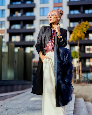 Woman wearing a Denim Tulle Detail Blazer with ruffle, styled elegantly against modern architecture.