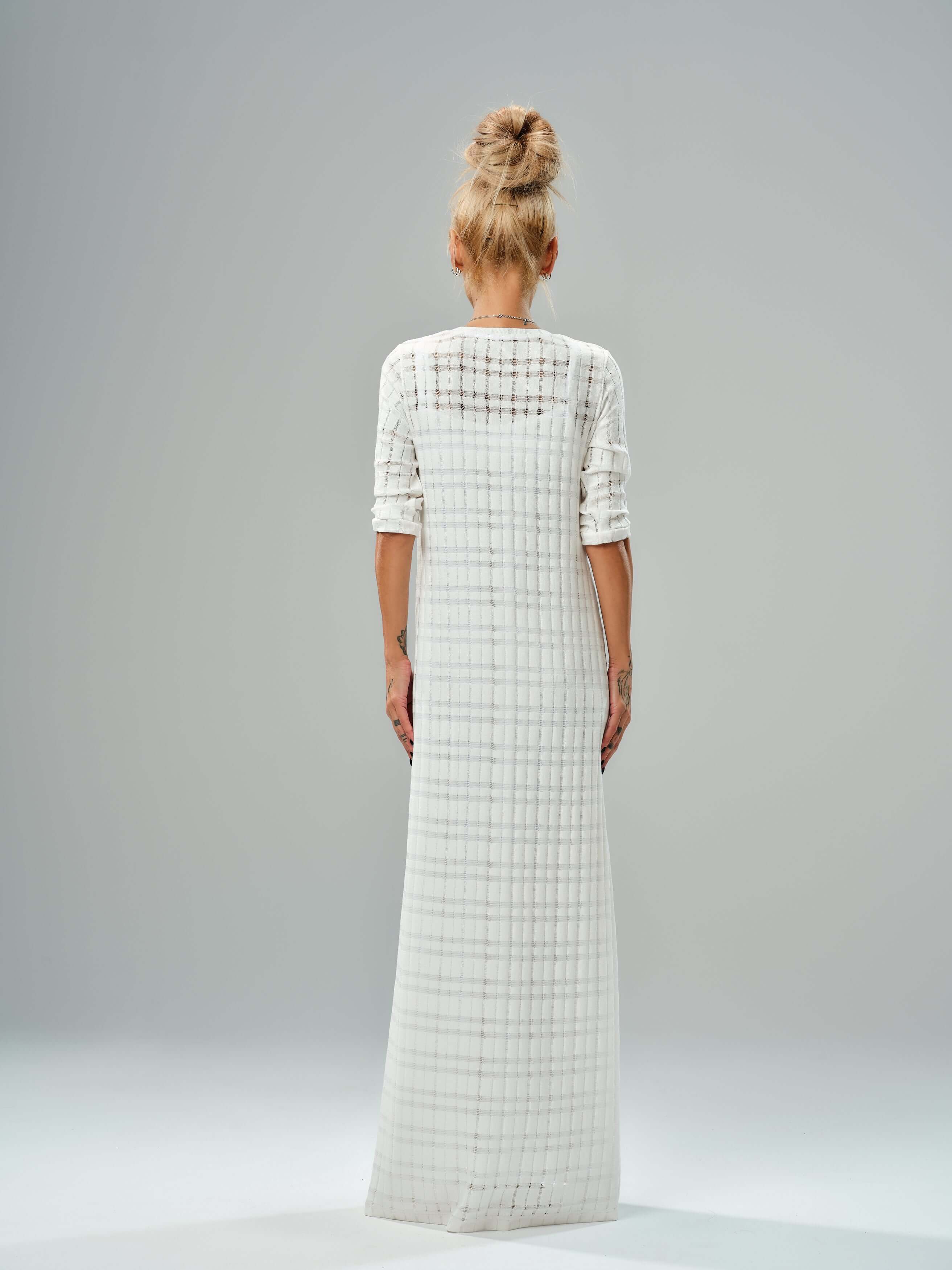 Back view of a long white knitted cotton dress with a semi-sheer texture and layered design, showcasing its elegant flow.