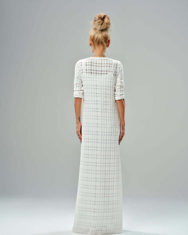 Back view of a long white knitted cotton dress with a semi-sheer texture and layered design, showcasing its elegant flow.