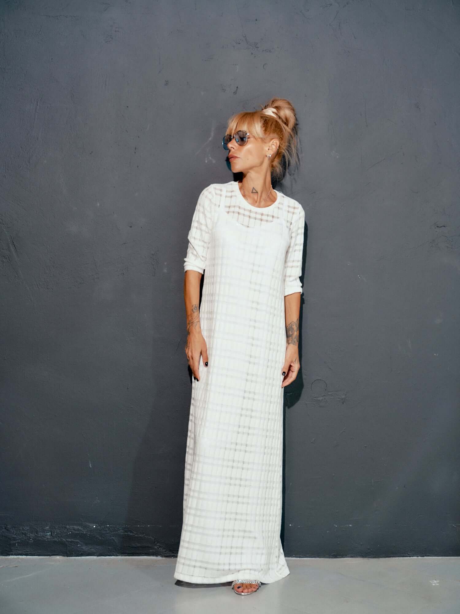 Elegant white knitted cotton dress with long sleeves and asymmetrical cut, showcased against a dark wall.