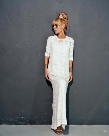 Model wearing a white knitted cotton dress with a sleek design against a dark background.