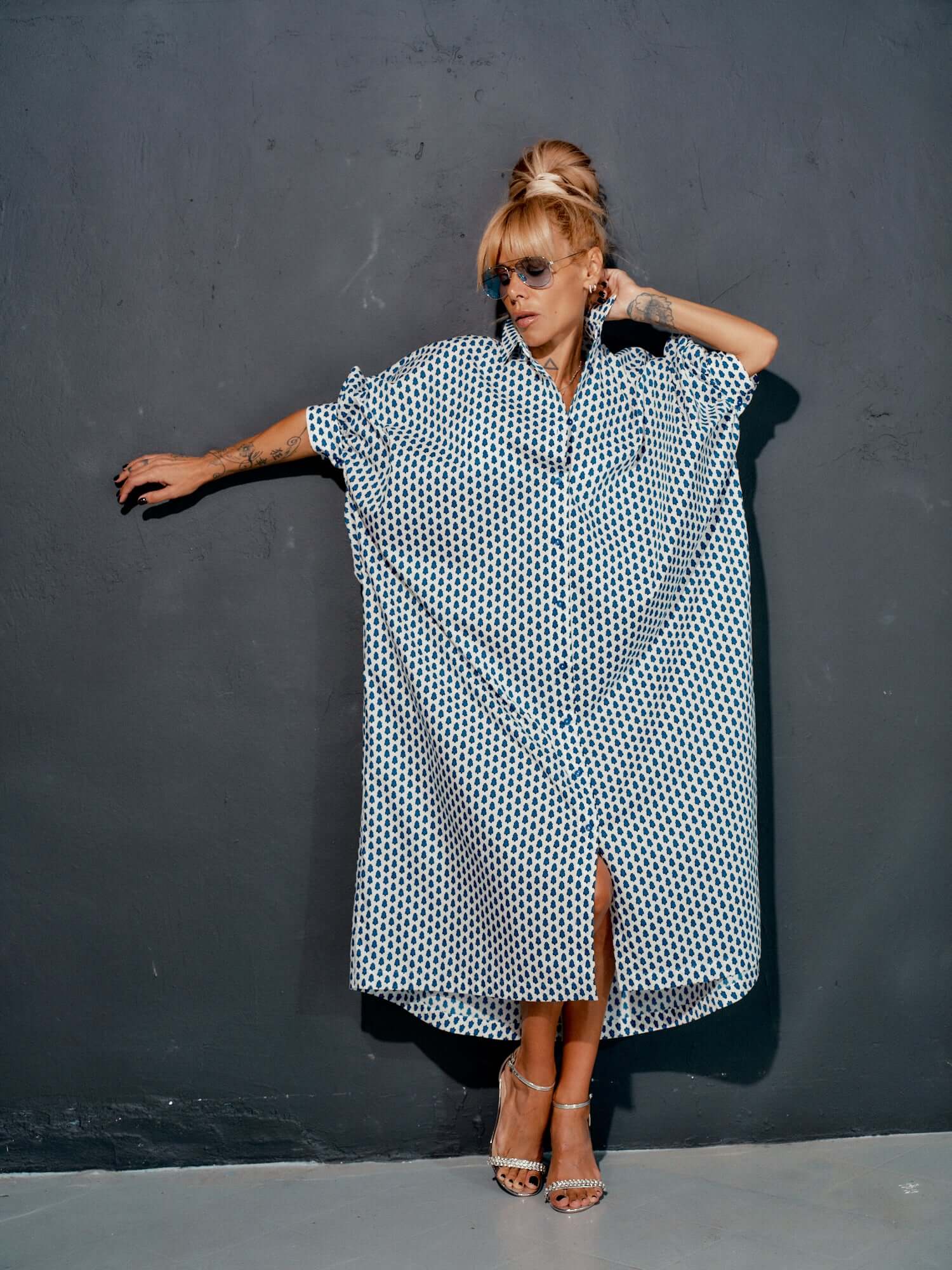 Woman wearing an oversized shirt dress with a blue micro floral print, styled with sunglasses against a dark wall.