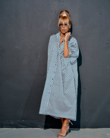 Woman in an oversized shirt dress with blue micro floral print, styled elegantly against a grey background.