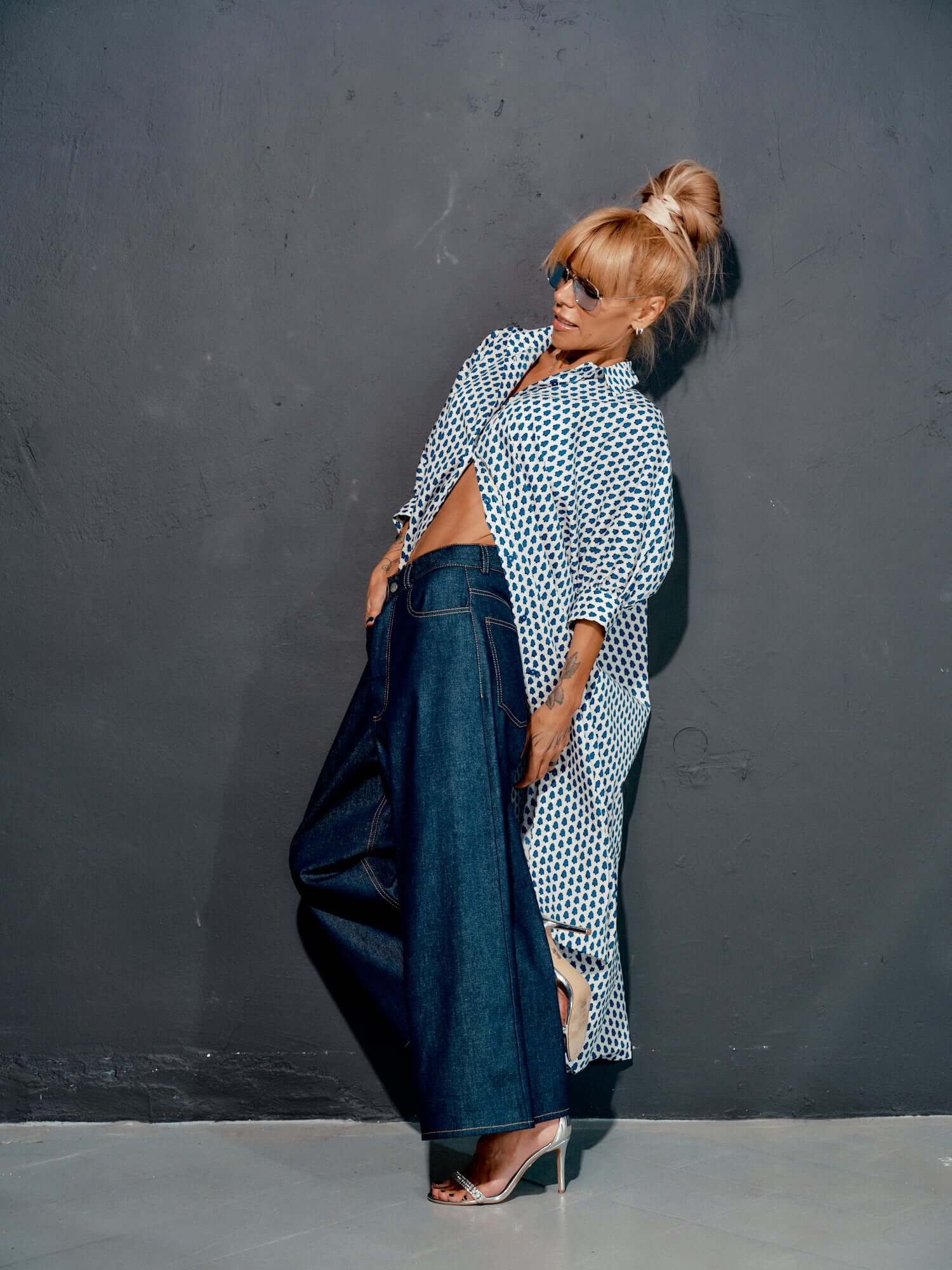 Fashion model wearing wide-leg denim jeans with a stylish top against a modern gray backdrop.