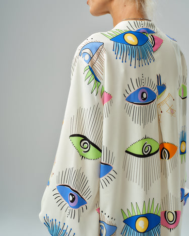 Side view of a model wearing a vibrant eye print shirt dress with a loose fit and ¾ sleeves.