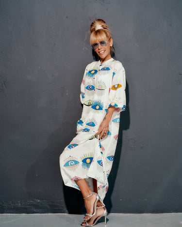 Model showcasing a vibrant eye print shirt dress with a loose fit and ¾ sleeves against a gray background.