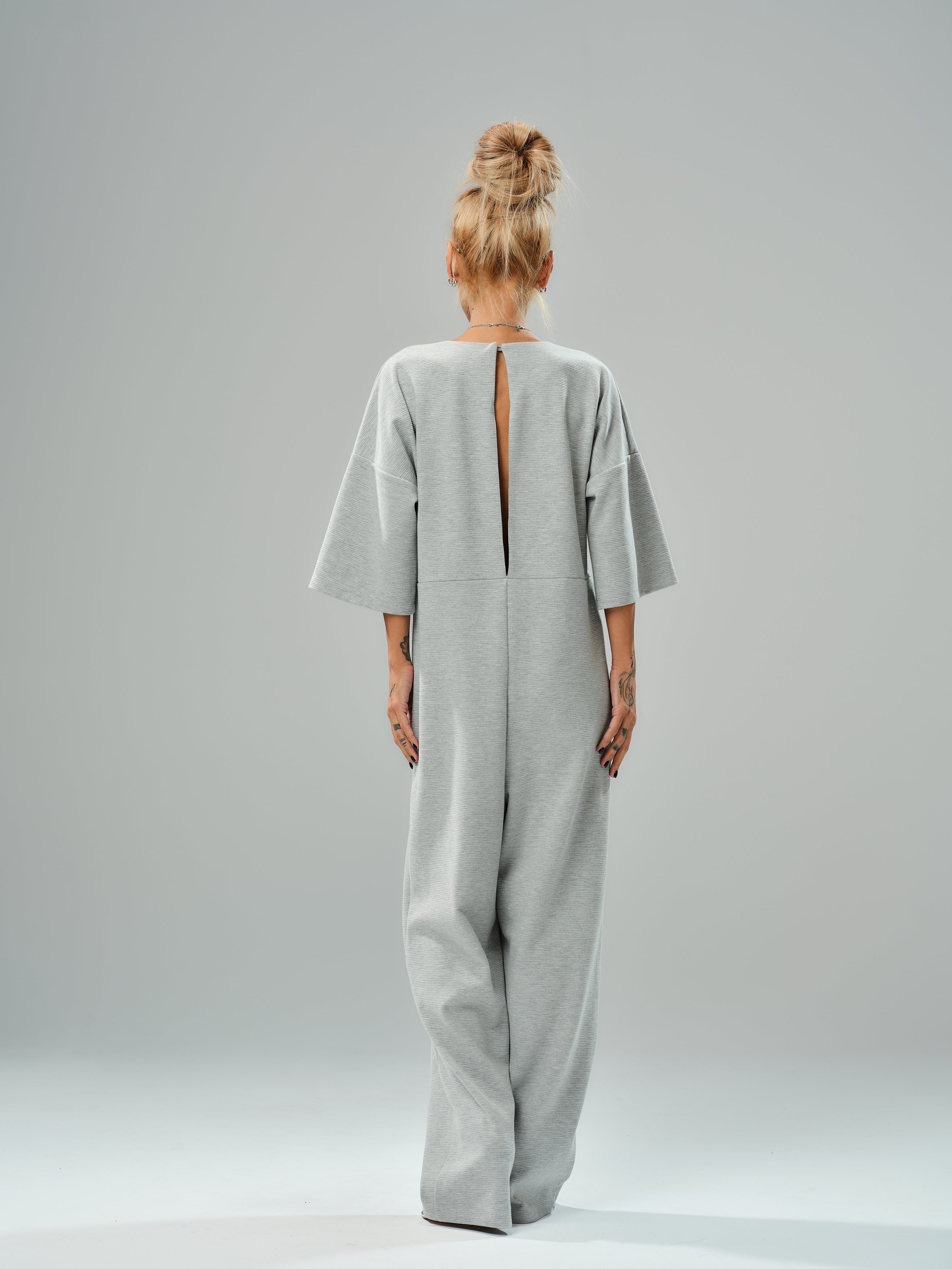 Grey wide-leg jumpsuit with open back, featuring cropped sleeves and relaxed fit, showcasing modern tailoring.