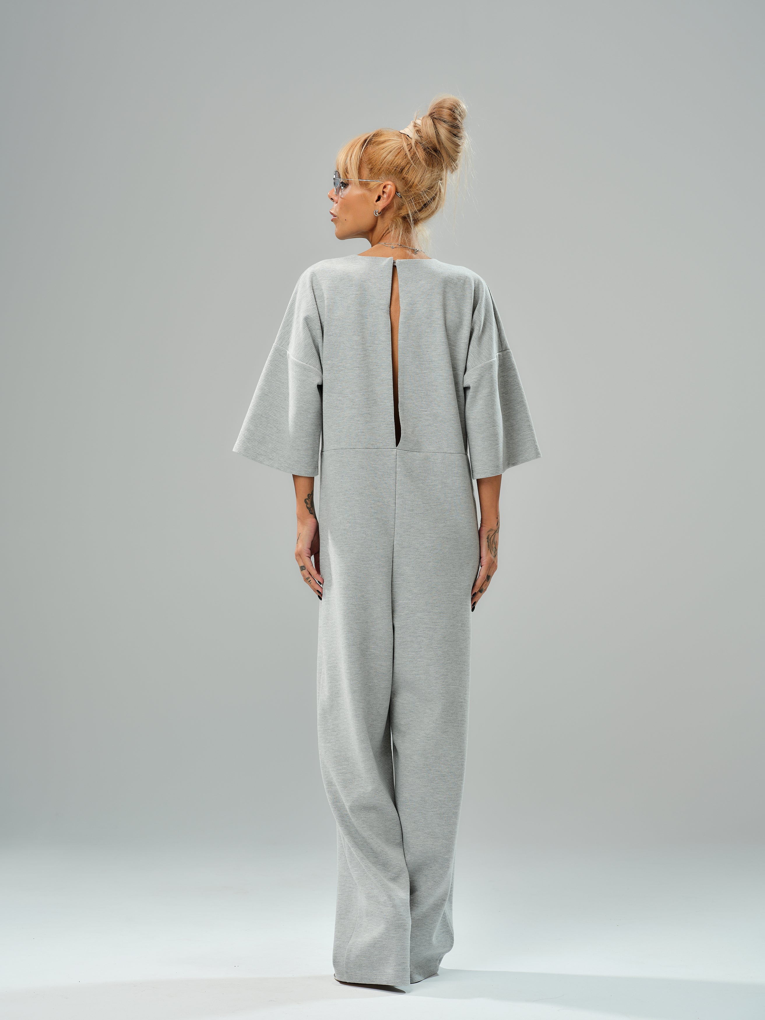 Grey wide-leg jumpsuit with open back, featuring cropped sleeves and a bold slit, showcasing modern style.