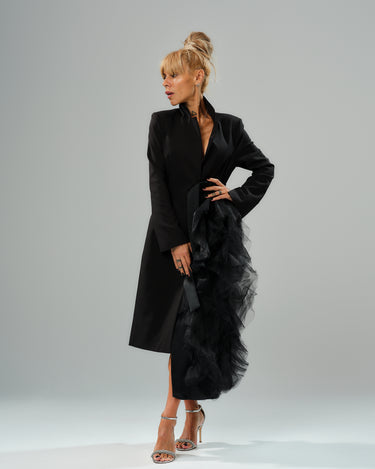 Elegant model showcasing a black tulle detail blazer with satin belt, dramatic tulle accent, and high collar.