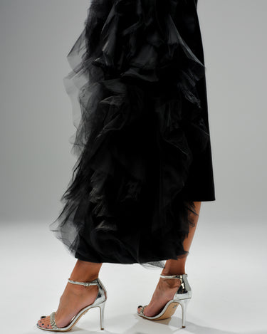 Side view of a model wearing a black tulle detail blazer with dramatic tulle accents and silver high-heeled sandals.