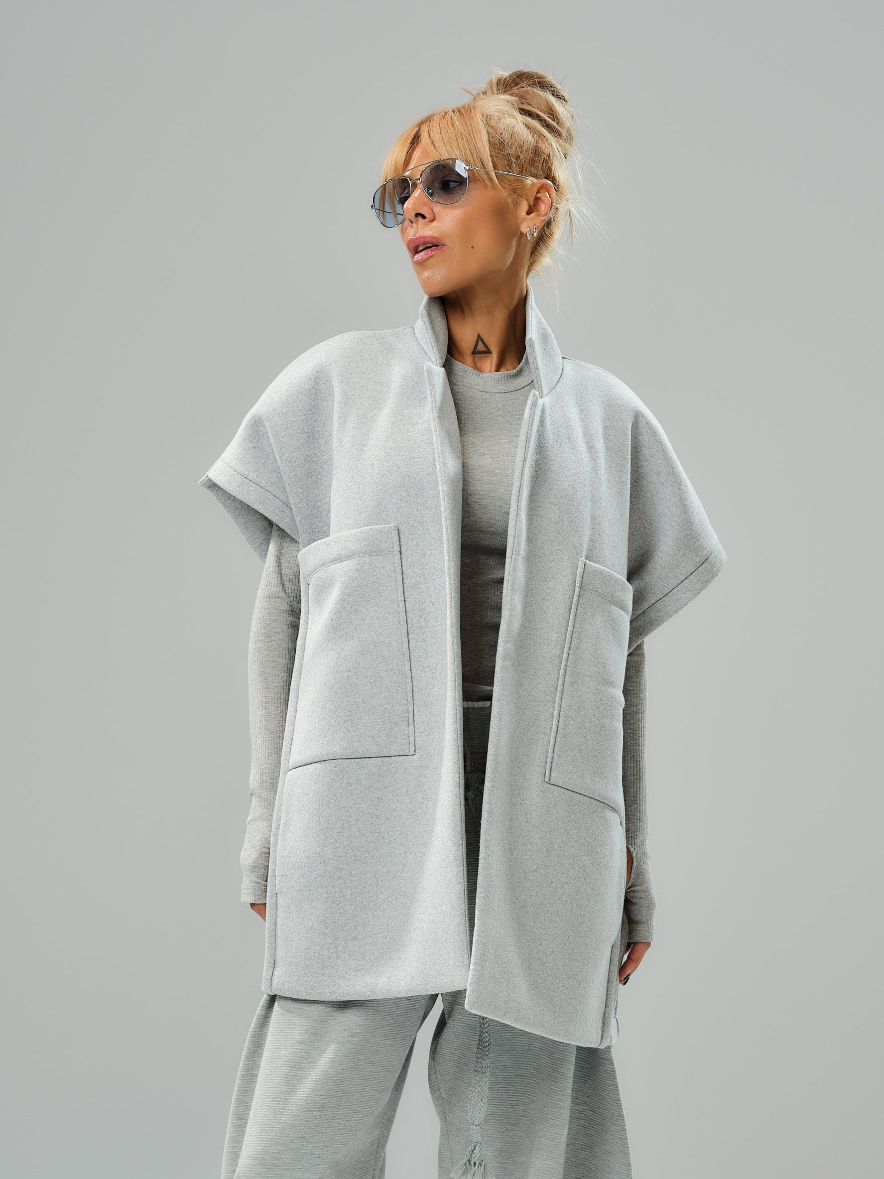 Model wearing a grey sleeveless coat with oversized pockets, styled for a modern casual look.