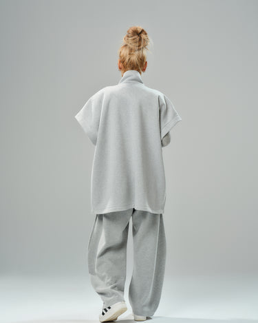 Back view of a woman wearing a grey sleeveless coat with oversized pockets and matching casual pants.