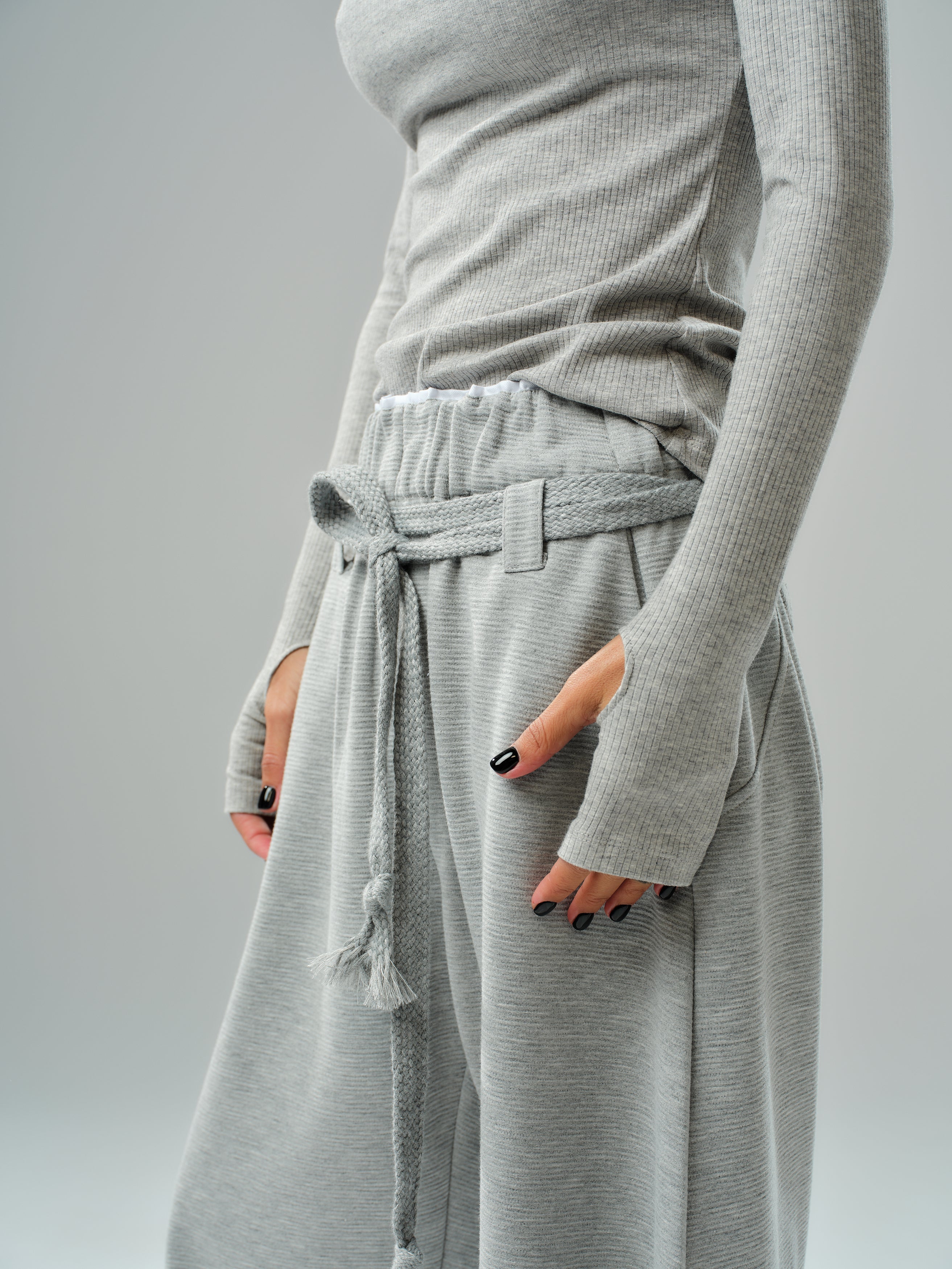 Model wearing oversized grey three-piece set featuring drawstring trousers and fitted long-sleeve top.