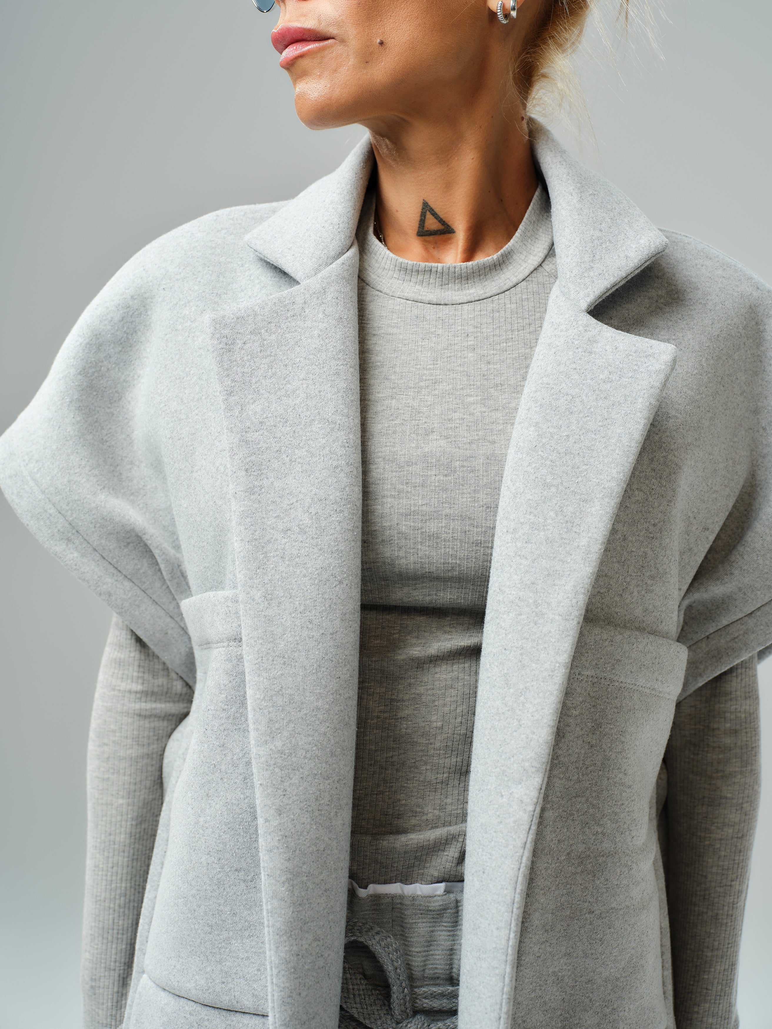 Model wearing a grey sleeveless coat over a matching top, showcasing modern streetwear style.