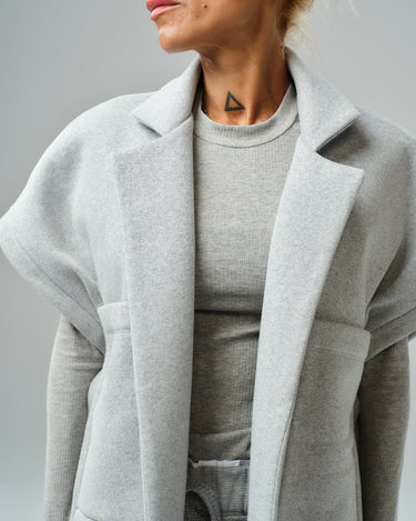 Model wearing a grey sleeveless coat over a matching top, showcasing modern streetwear style.