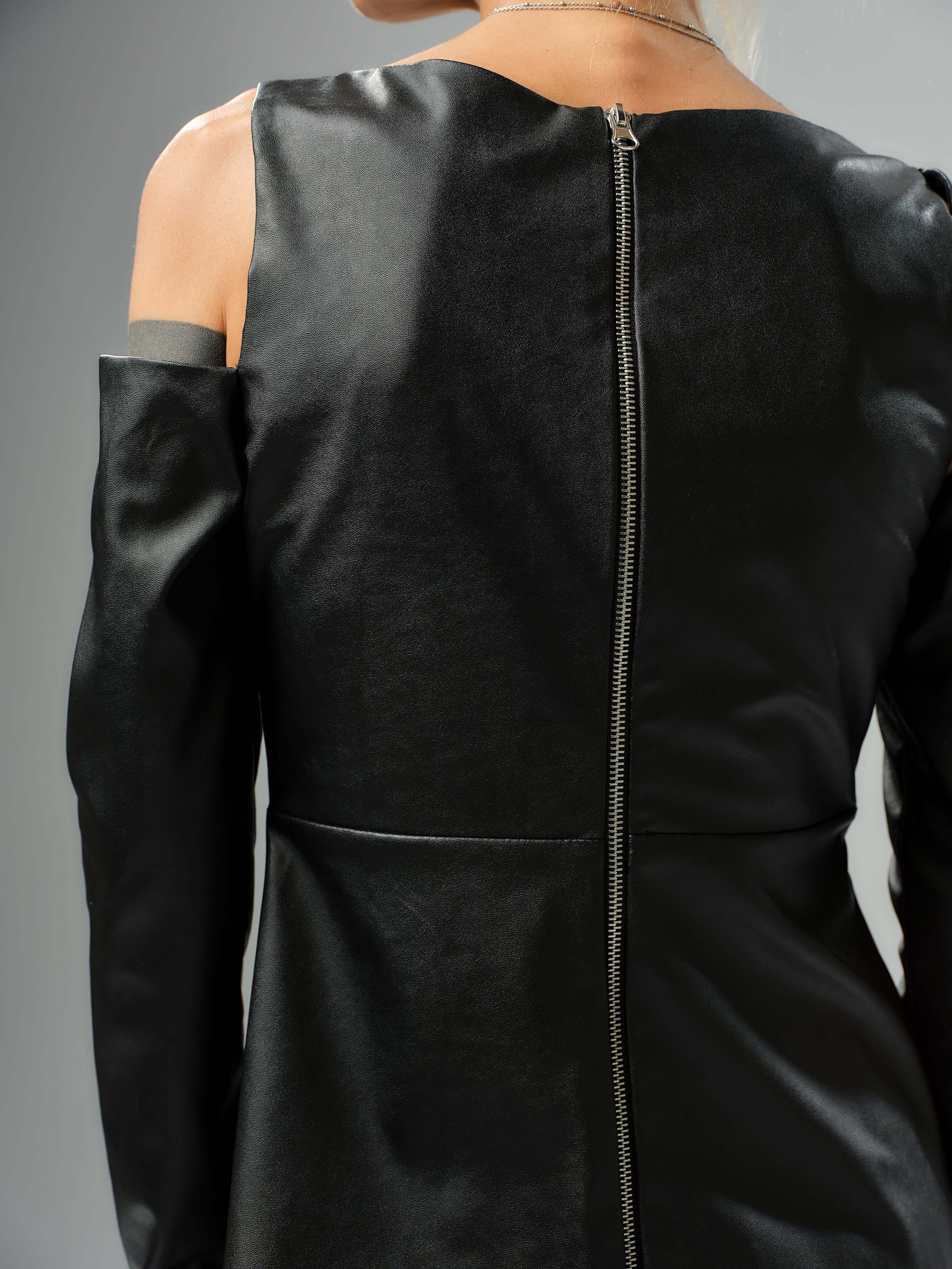 Back view of a black faux leather top with cut-out shoulder details and a zipper closure, highlighting its modern design.