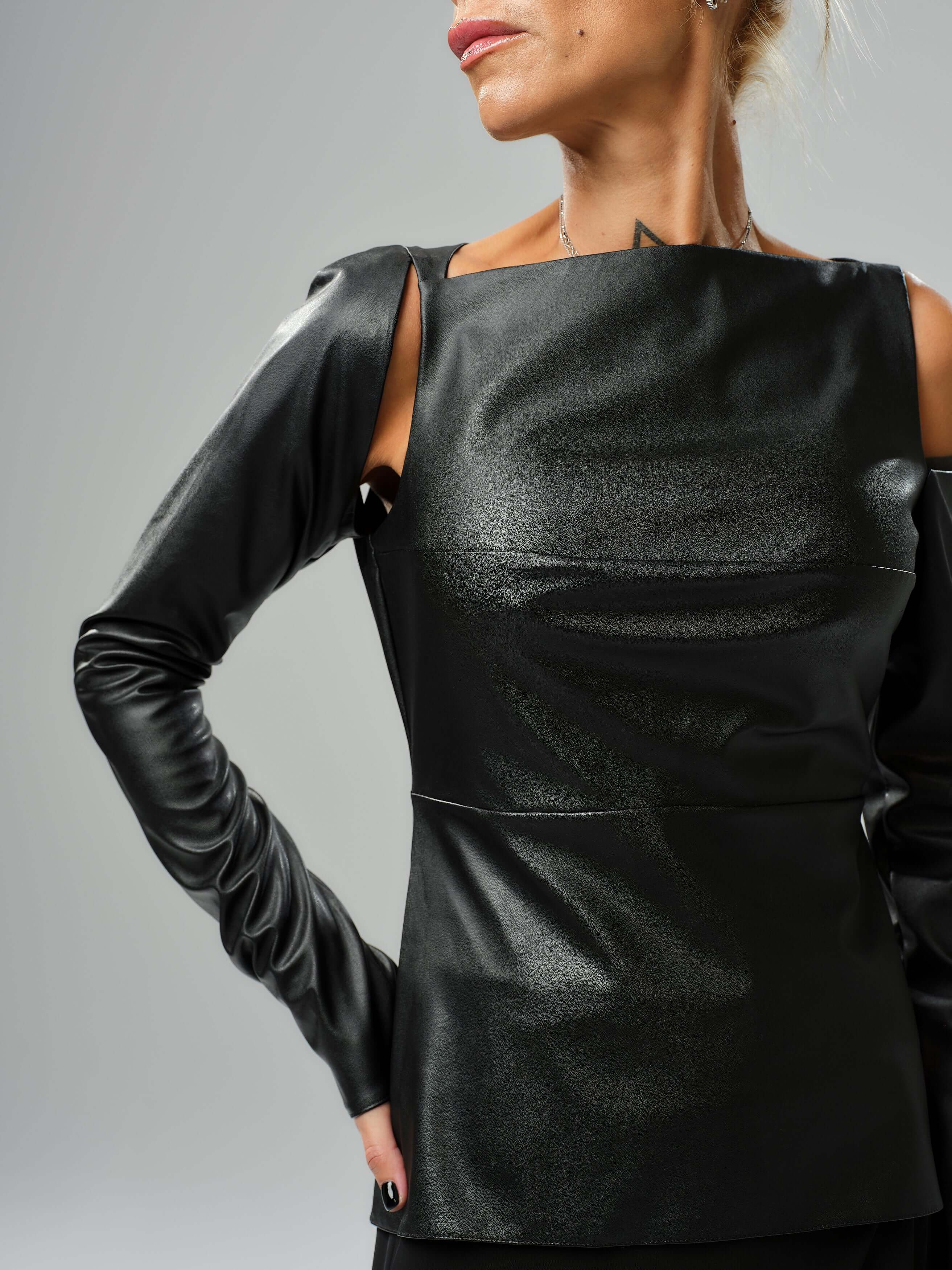 Stylish black faux leather top featuring cut-out shoulder details and structured silhouette, perfect for modern outfits.