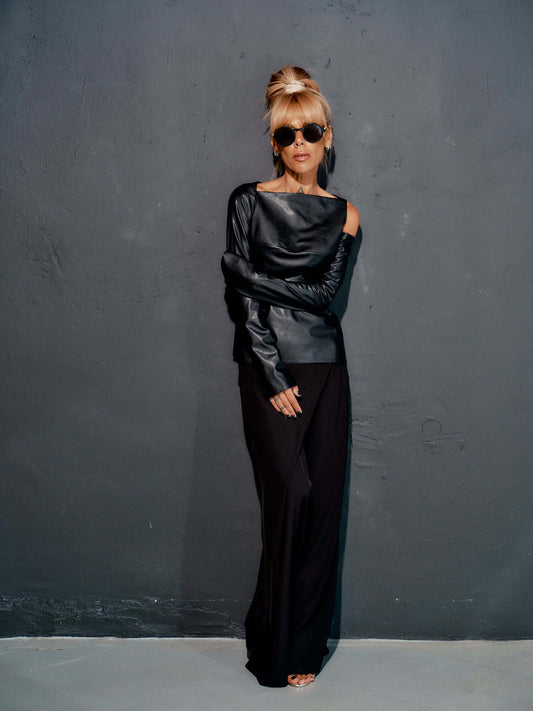 Elegant model in black wide-leg pants and stylish off-shoulder top, showcasing modern fashion against a gray wall.