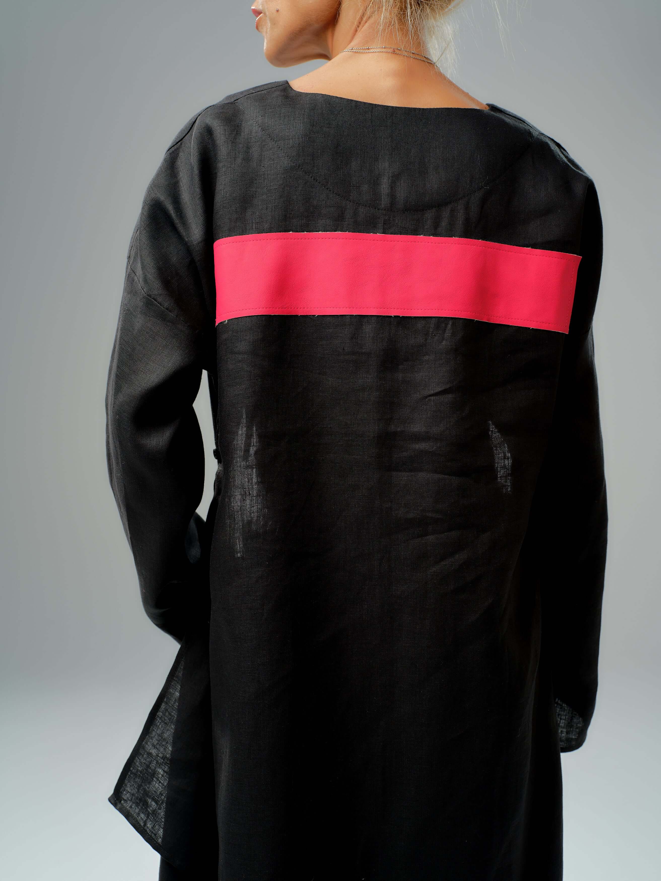 Back view of a black tunic featuring a striking red leather stripe, showcasing modern and minimalistic design.
