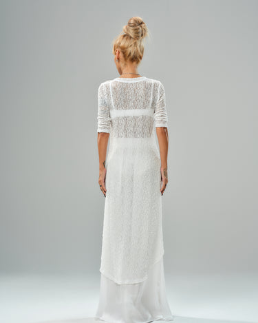 Back view of a woman in a white textured tunic and flowing maxi skirt, showcasing an elegant contemporary look.